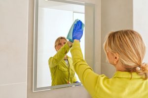 Una mujer está limpiando el espejo del baño montado en la pared.