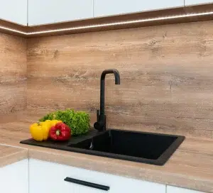 Wastafel dapur lubang tunggal berwarna hitam dan keran dengan sayuran di sampingnya