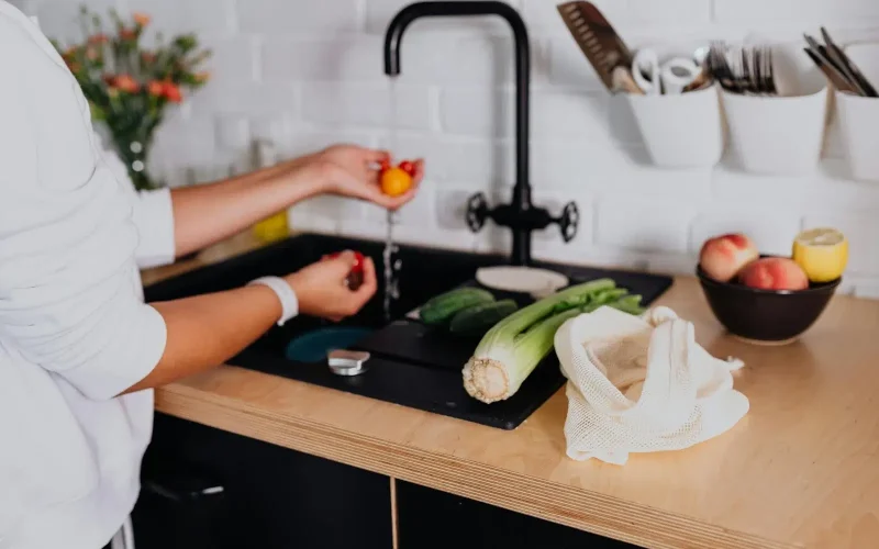 Seorang wanita sedang mencuci di wastafel dapur dengan keran